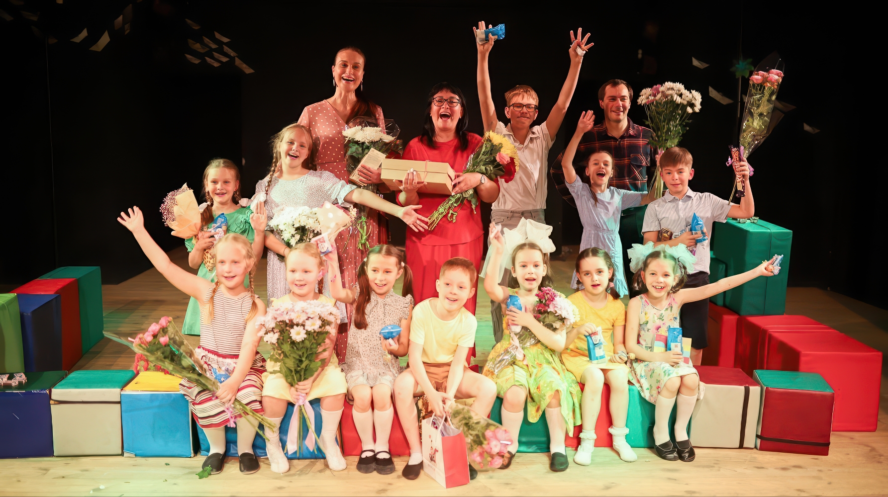 Дети на сцене на цветных кубах с цветами